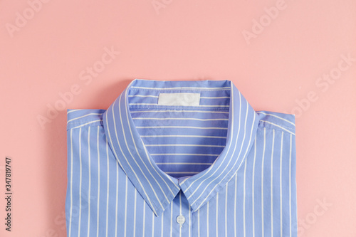 One perfectly folded buttoned shirt with striped pattern. Single piece of formal wear with blank label isolated on pink background. Close up, top view, copy space.