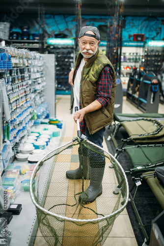 Fototapeta Naklejka Na Ścianę i Meble -  Happy angler holds net in fishing shop