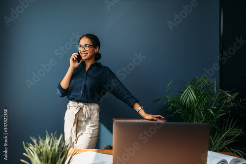Happy entrepreneur leaning to a chair and looking away while talking on mobile phone