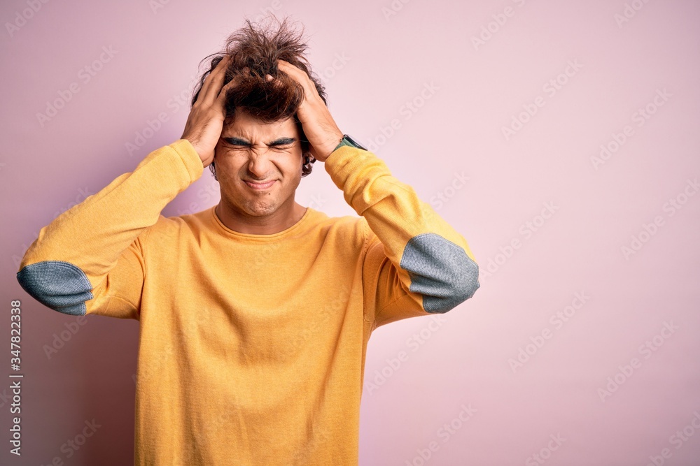 Young handsome man wearing yellow casual t-shirt standing over isolated pink background suffering from headache desperate and stressed because pain and migraine. Hands on head. Young handsome man wearing yellow casual t-shirt standing over isolated pink background suffering from headache desperate and stressed because pain and migraine. Hands on head.