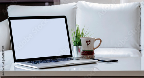 Mockup blank screen laptop with smartphone  mug and houseplant on white wooden top table in living room.
