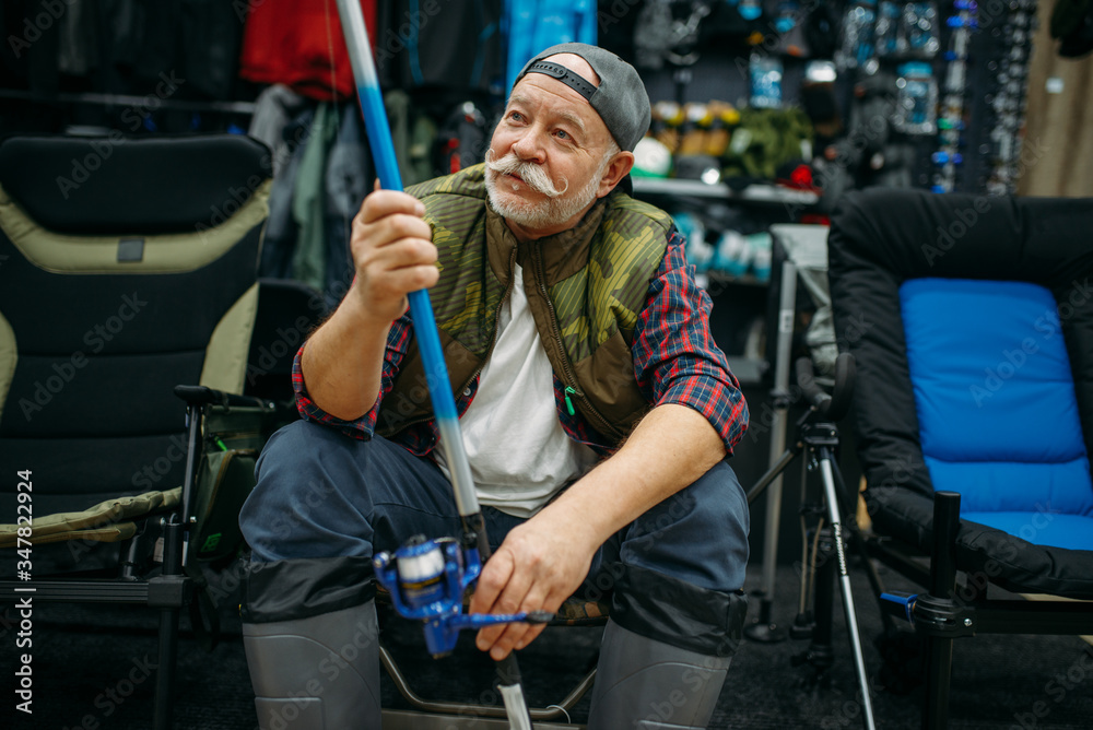Angler in rubber boots holds rod in fishing shop Angler in rubber boots holds rod in fishing shop