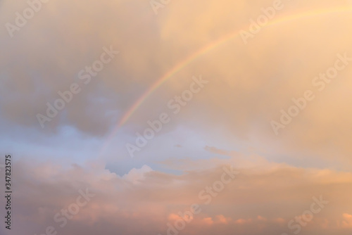 A beautiful rainbow in the sky at sunset with glowing pink clouds.