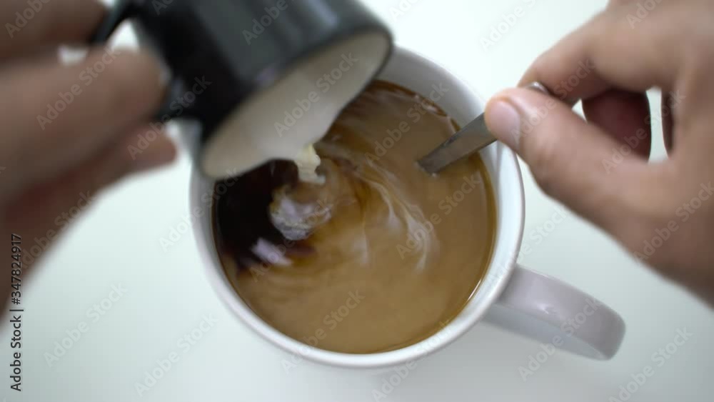 Top view and close up of person male hands put the milk into the white coffee cup and stirring coffee with spoon. 4k resolution. Top view and close up of person male hands put the milk into the white coffee cup and stirring coffee with spoon. 4k resolution.