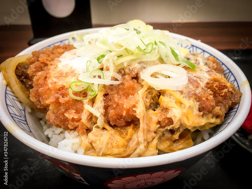 Katsudon, a bowl of rice topped with a deep-fried pork cutlet, egg, vegetables, and condiments, with Tsukemono pickles on the table in local restaurant in Japan.
