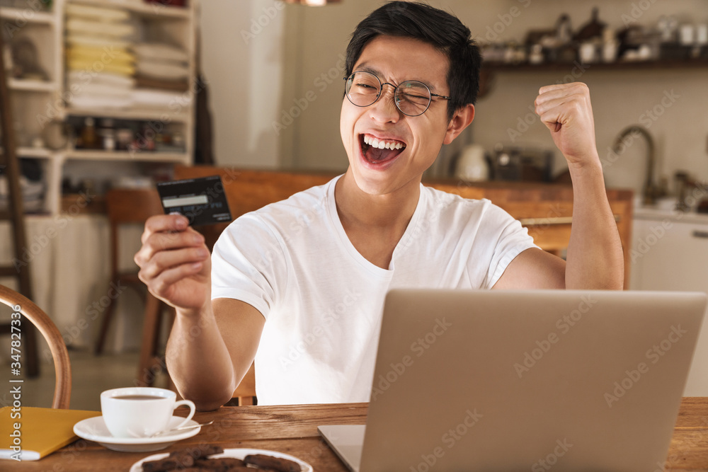 Image of asian man making winner gesture while holding credit card