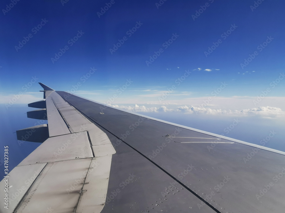 View of a wing and distant clouds from the window of an airplane at cruising altitude.