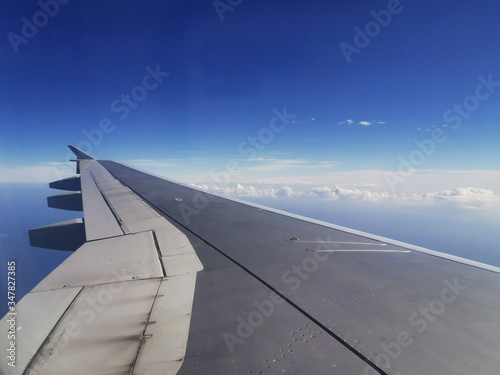 View of a wing and distant clouds from the window of an airplane at cruising altitude.