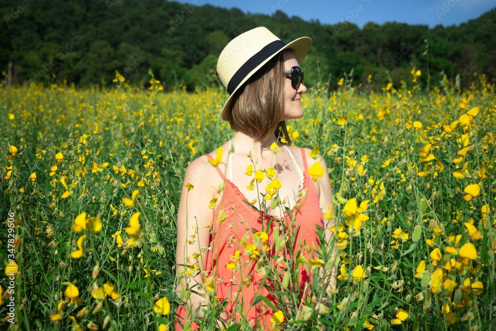 Fototapeta premium Smiling young woman enjoying her time outside in green yellow flowers field. Concept of happy, harmony life style. Summer time.