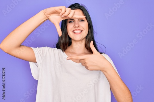Young beautiful brunette woman wearing casual white t-shirt over purple background smiling making frame with hands and fingers with happy face. Creativity and photography concept.