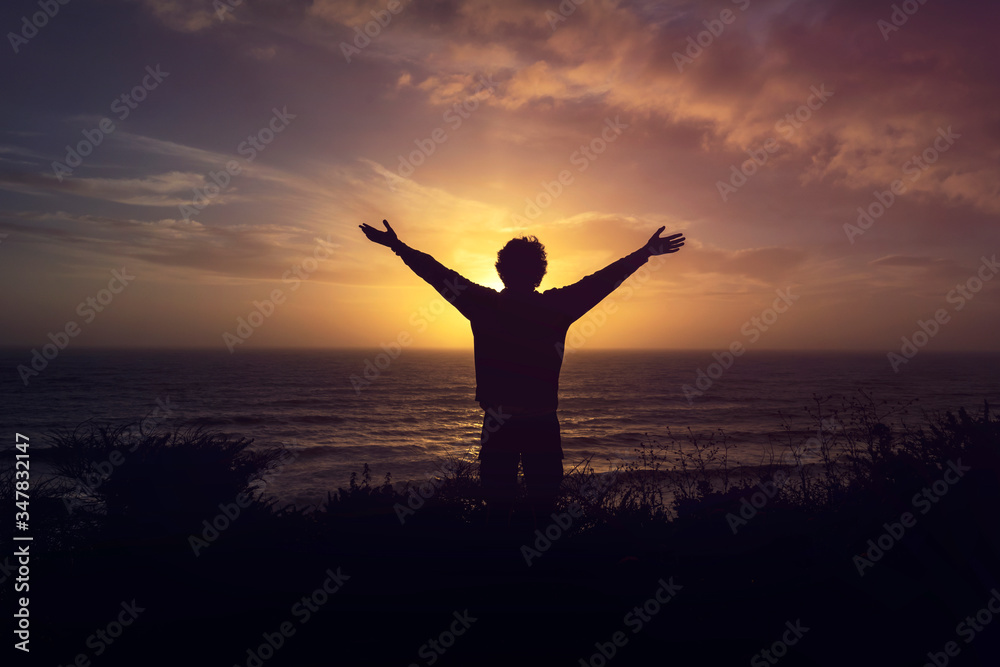 Silhouette Of A Man Watching orange Sunset on cliff over the sea with open arms