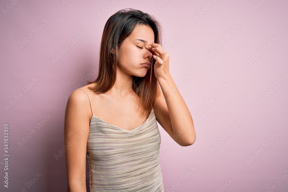 Young beautiful brunette girl wearing casual striped t-shirt over isolated pink background tired rubbing nose and eyes feeling fatigue and headache. Stress and frustration concept. Young beautiful brunette girl wearing casual striped t-shirt over isolated pink background tired rubbing nose and eyes feeling fatigue and headache. Stress and frustration concept.