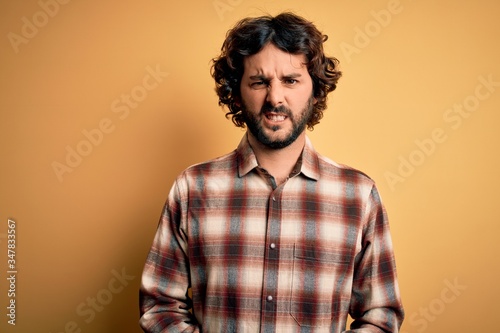 Young handsome man with beard wearing casual shirt standing over yellow background skeptic and nervous, frowning upset because of problem. Negative person.
