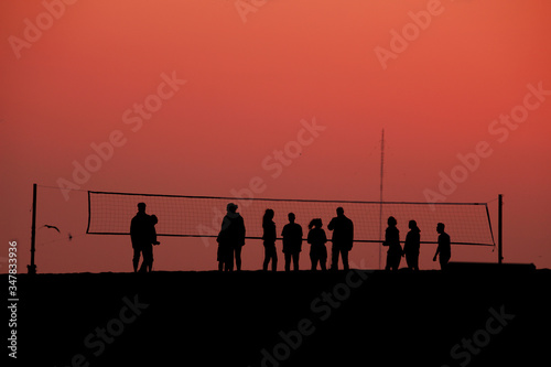 silhouettes of people playing volleyball in the evening on the beach at sunset