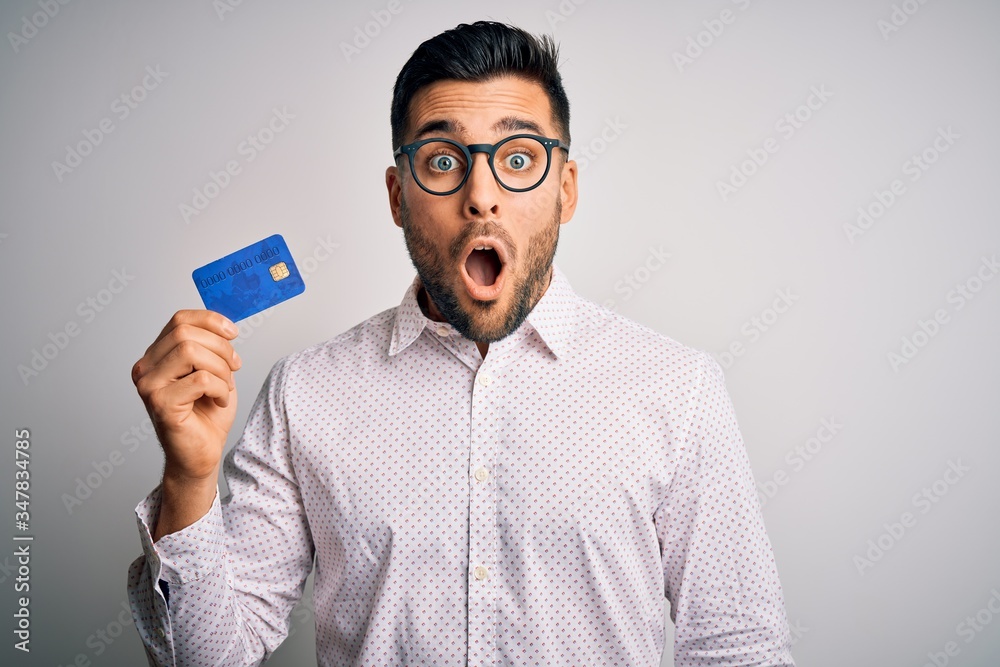 Young business man holding credit card over isolated background scared in shock with a surprise face, afraid and excited with fear expression - obrazy, fototapety, plakaty 