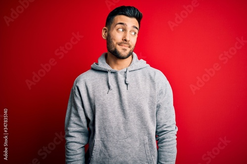 Young handsome sportsman wearing sweatshirt standing over isolated red background smiling looking to the side and staring away thinking.