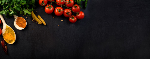 Food background with colorful food ingredients border from above. Top view of parsley, cherry tomato, herbs and spices on rustic black table.