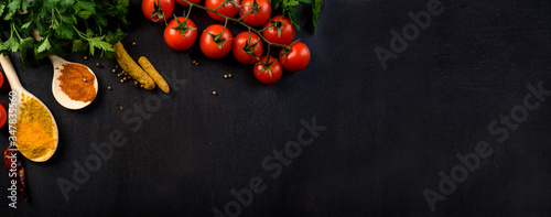 Food background with colorful food ingredients border from above. Top view of parsley, cherry tomato, herbs and spices on rustic black table.