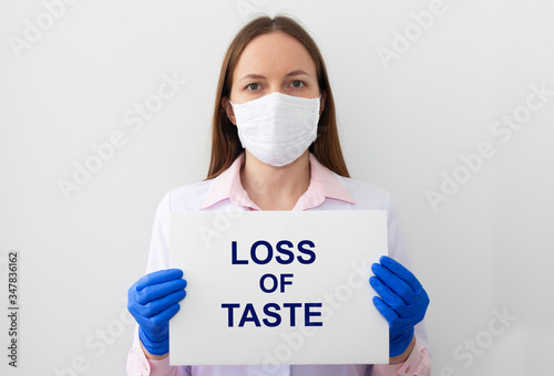 LOSS OF TASTE text as a symptom of disease. text on white paper in hands in protective gloves with doctor on white background photo