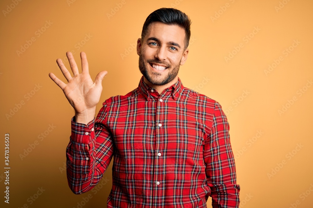Young handsome man wearing casual shirt standing over isolated yellow background showing and pointing up with fingers number five while smiling confident and happy. Young handsome man wearing casual shirt standing over isolated yellow background showing and pointing up with fingers number five while smiling confident and happy.