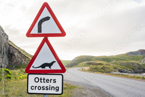 Dangerous right curve and Otters crossing ahead. Red warning road sign along a highway in the scottish highlands. Scotland, UK, on a cloudy day photo