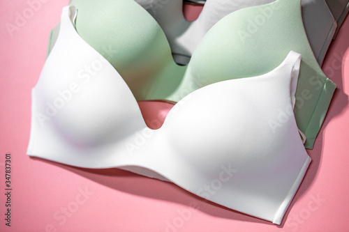 Many women's bra of beige, white, green and gray colors on pink plastic background. Underwear fashion. Basic lingerie. Classic bra photo
