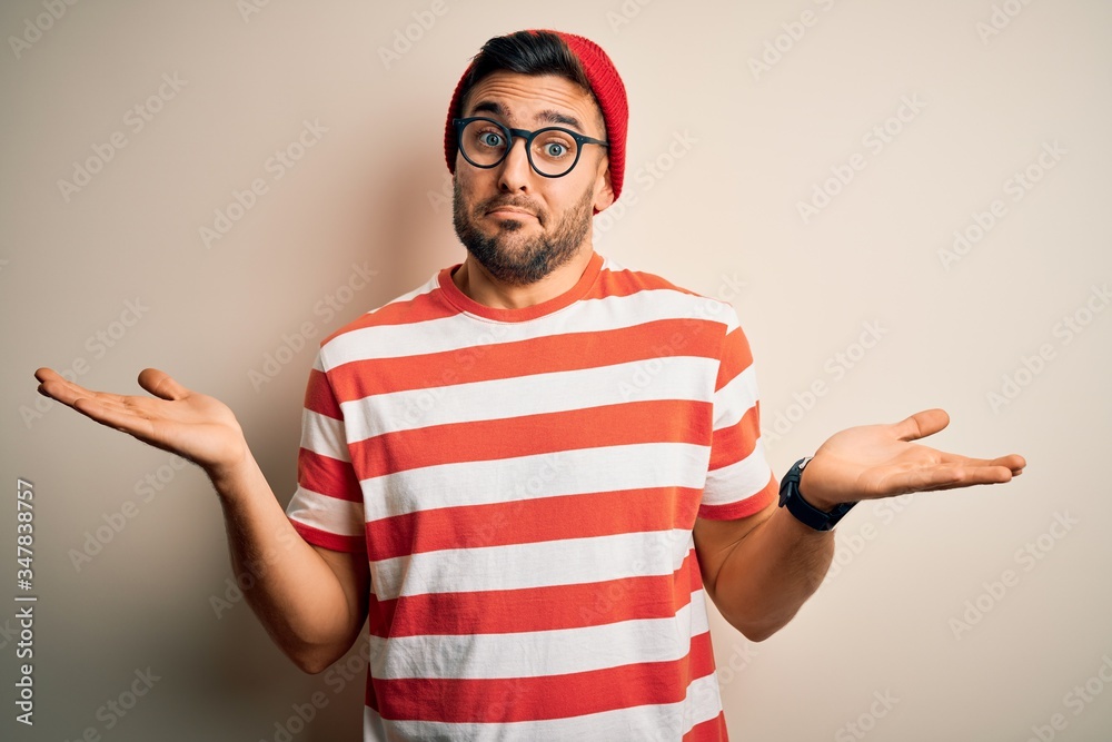 Young handsome man wearing casual striped t-shirt and glasses over white background clueless and confused expression with arms and hands raised. Doubt concept. Young handsome man wearing casual striped t-shirt and glasses over white background clueless and confused expression with arms and hands raised. Doubt concept.