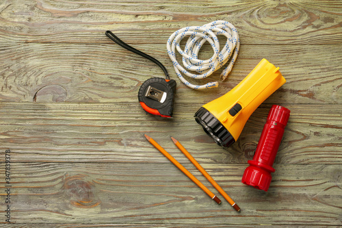 Modern flashlights with rope, tape measure and pencils on wooden background
