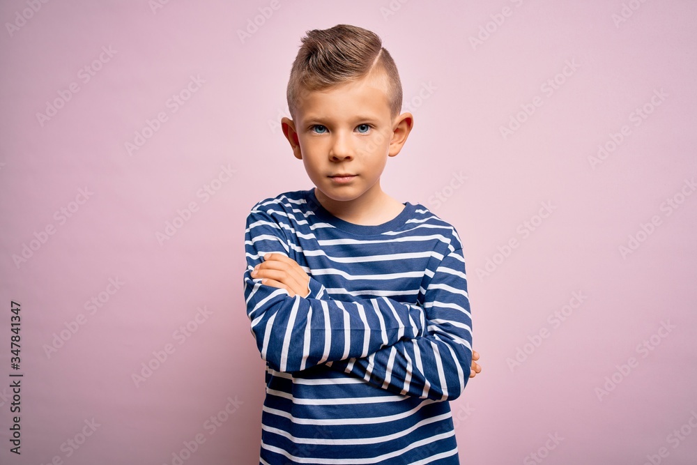Young little caucasian kid with blue eyes wearing nautical striped shirt over pink background skeptic and nervous, disapproving expression on face with crossed arms. Negative person. Young little caucasian kid with blue eyes wearing nautical striped shirt over pink background skeptic and nervous, disapproving expression on face with crossed arms. Negative person.