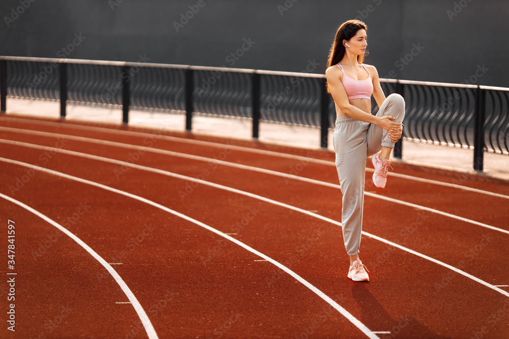 Obraz premium Fitness sporty woman runner stretching legs before run on the stadium