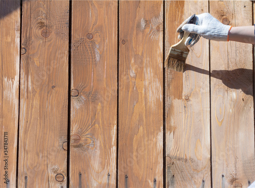 Processing of the wooden wall outside.A man's hand in a glove paint the wooden walls of a gazebo or veranda with a brush.