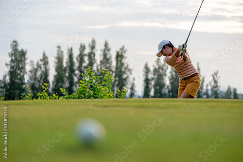 Asian golfer woman golf player hitting chips golf ball to the hole on the green. People with golf course at golf club in the sunny day. Hobby in holiday vacations Sport Concept