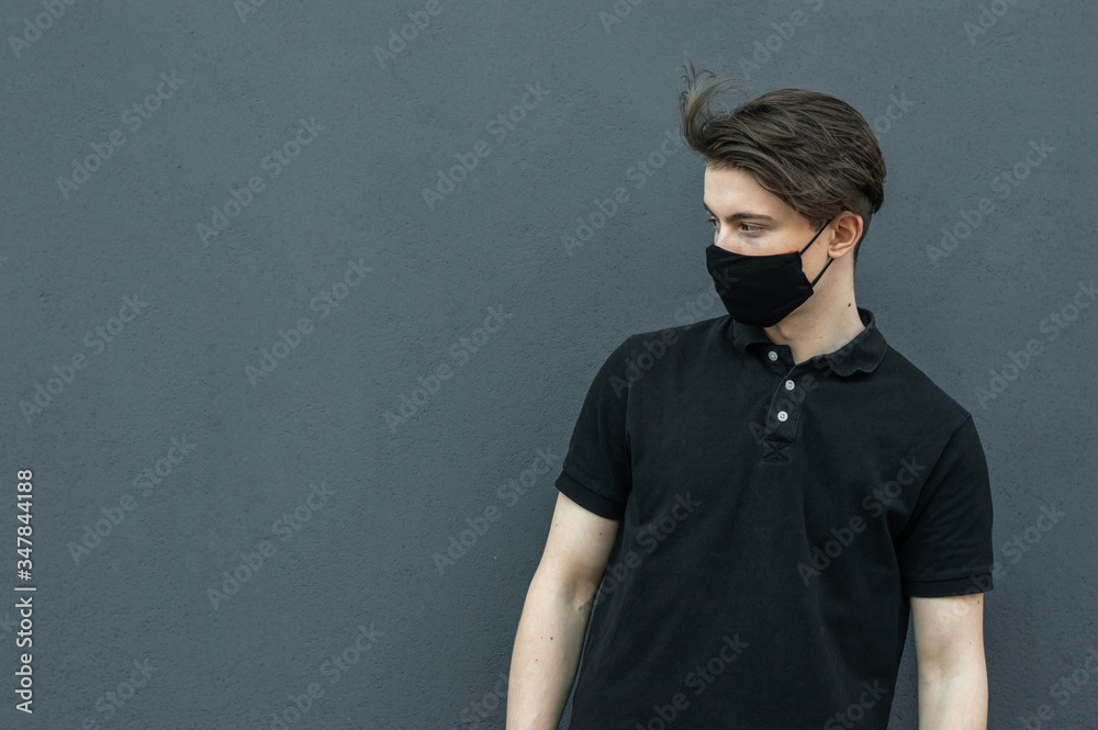 Portrait of guy in black t-shirt and black medical mask on his face on dark gray background for protect and stop viruses and coronavirus pandemic, covid-19 outbreak Portrait of guy in black t-shirt and black medical mask on his face on dark gray background for protect and stop viruses and coronavirus pandemic, covid-19 outbreak