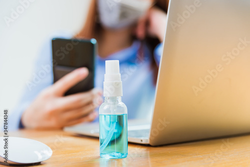 Asian young business woman wearing face mask protective using smart mobile phone for reading SMS message near laptop computer at home office quarantines disease coronavirus or COVID-19  work from home