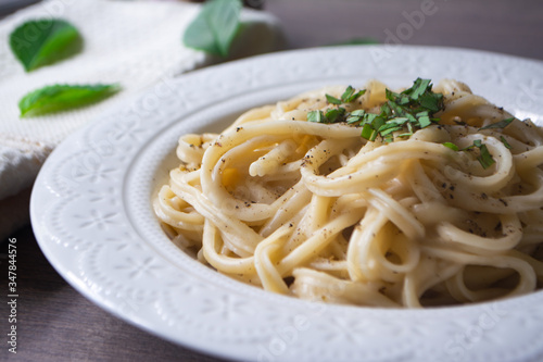 A vegan version of traditional Italian pasta fettuccine alfredo with creamy white sauce garnished with basil on a wooden surface with a fork, napkin, garlic and basil leaves
