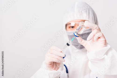 Fototapeta Naklejka Na Ścianę i Meble -  Asian female woman doctor or nurse in PPE uniform and gloves wearing face mask protective in the laboratory holding needle syringe drug and medicine vial vaccine bottle, Health medical concept