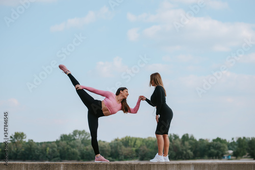 Two attractive young caucasian women are exercising by the river. Training in nature