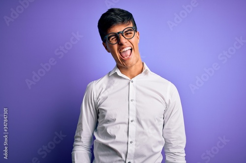 Young handsome business man wearing shirt and glasses over isolated purple background winking looking at the camera with sexy expression, cheerful and happy face.