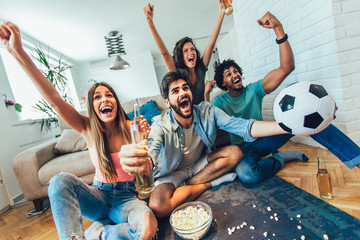Very excited friends having fun by watching football match and eating at home, indoors. Friendship, leasure, rest, home party concept