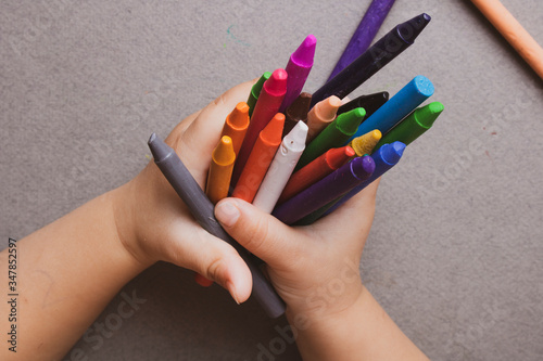 Closeup of child's hands with colorful wax crayons pencils. learning concept. Flat lay