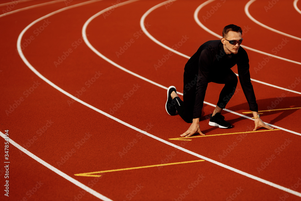 Young athlete man wearing black tracksuit getting ready to run in the stadium