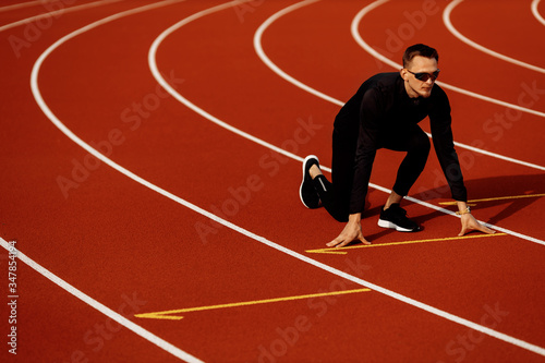 Young athlete man wearing black tracksuit getting ready to run in the stadium