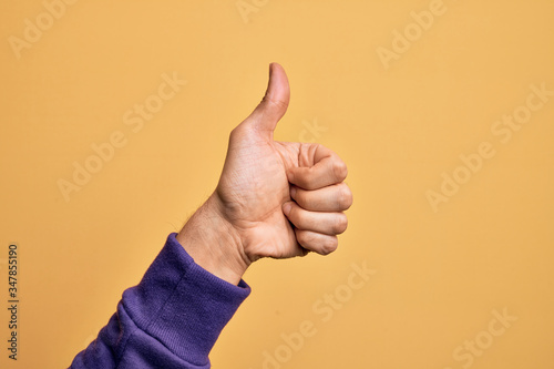 Hand of caucasian young man showing fingers over isolated yellow background doing successful approval gesture with thumbs up, validation and positive symbol photo