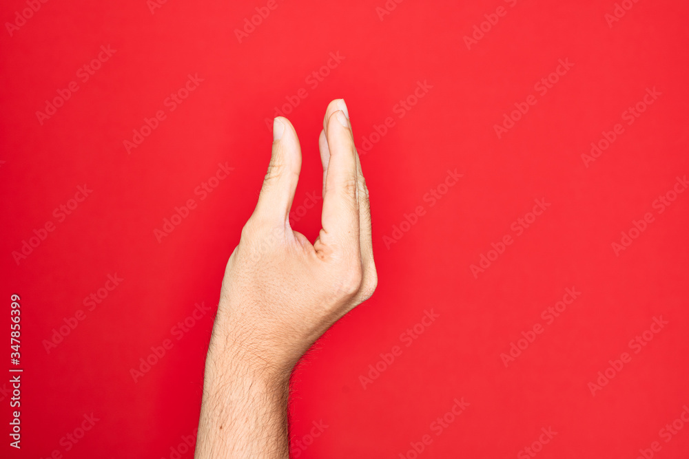 Hand of caucasian young man showing fingers over isolated red background picking and taking invisible thing, holding object with fingers showing space Hand of caucasian young man showing fingers over isolated red background picking and taking invisible thing, holding object with fingers showing space