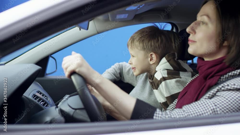 Brunette woman in casual clothes is driving car with greenscreen background. She is sitting in her car with her son on the bluesceen background isolated. She and her children are having a video chat Brunette woman in casual clothes is driving car with greenscreen background. She is sitting in her car with her son on the bluesceen background isolated. She and her children are having a video chat