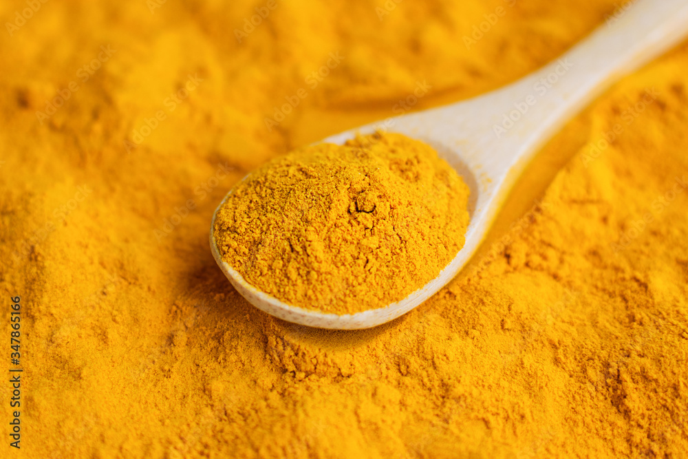Close-up turmeric powder in wooden spoon at scattered curcuma. Close-up turmeric powder in wooden spoon at scattered curcuma.