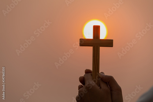 Both hands grasped the cross to pray to God. While the sun is setting or rising Christian religious concepts, the crucifixion of faith and faith in God.