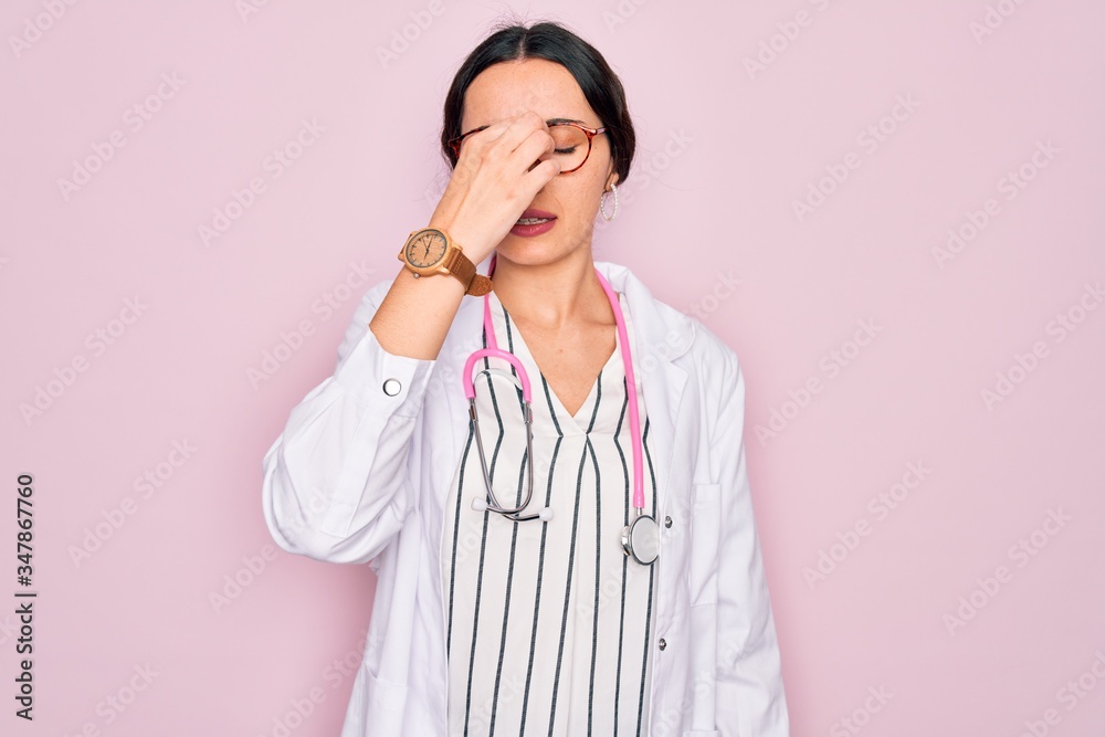 Beautiful doctor woman with blue eyes wearing coat and stethoscope over pink background tired rubbing nose and eyes feeling fatigue and headache. Stress and frustration concept. Beautiful doctor woman with blue eyes wearing coat and stethoscope over pink background tired rubbing nose and eyes feeling fatigue and headache. Stress and frustration concept.