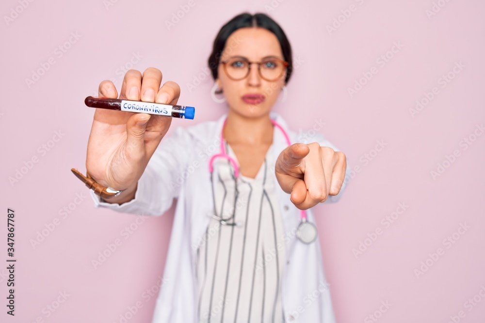Beautiful doctor woman with blue eyes wearing stethoscope holding coronavirus test tube pointing with finger to the camera and to you, hand sign, positive and confident gesture from the front Beautiful doctor woman with blue eyes wearing stethoscope holding coronavirus test tube pointing with finger to the camera and to you, hand sign, positive and confident gesture from the front