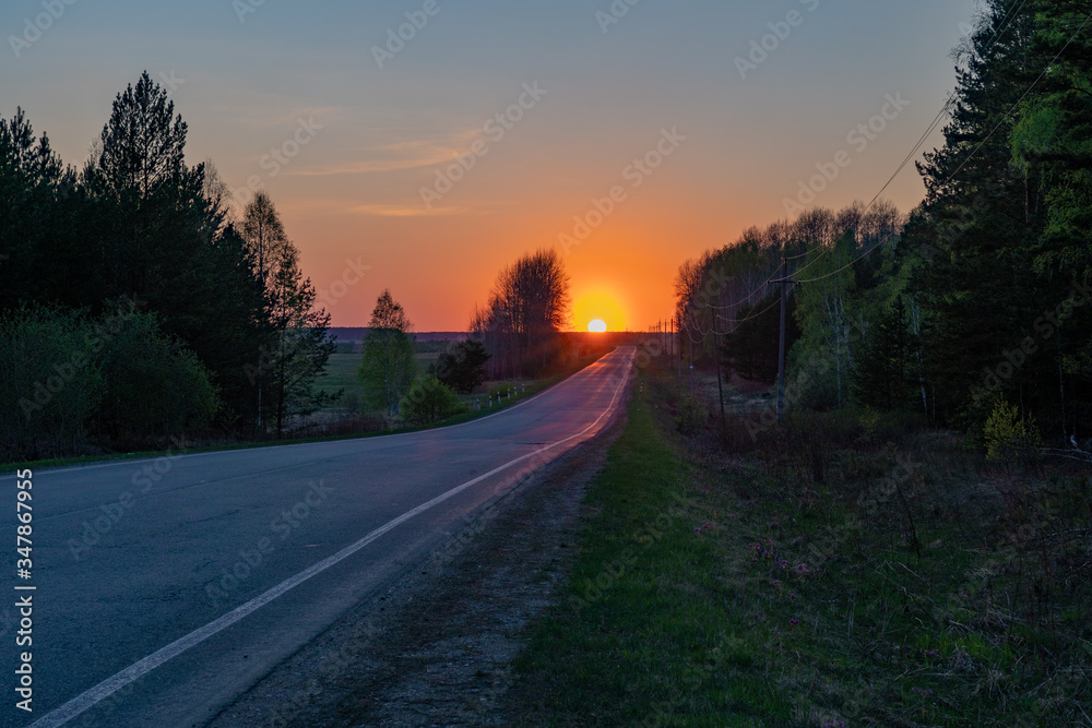 Picturesque rural landscape showing bright orange sunset over the road in the forest in spring